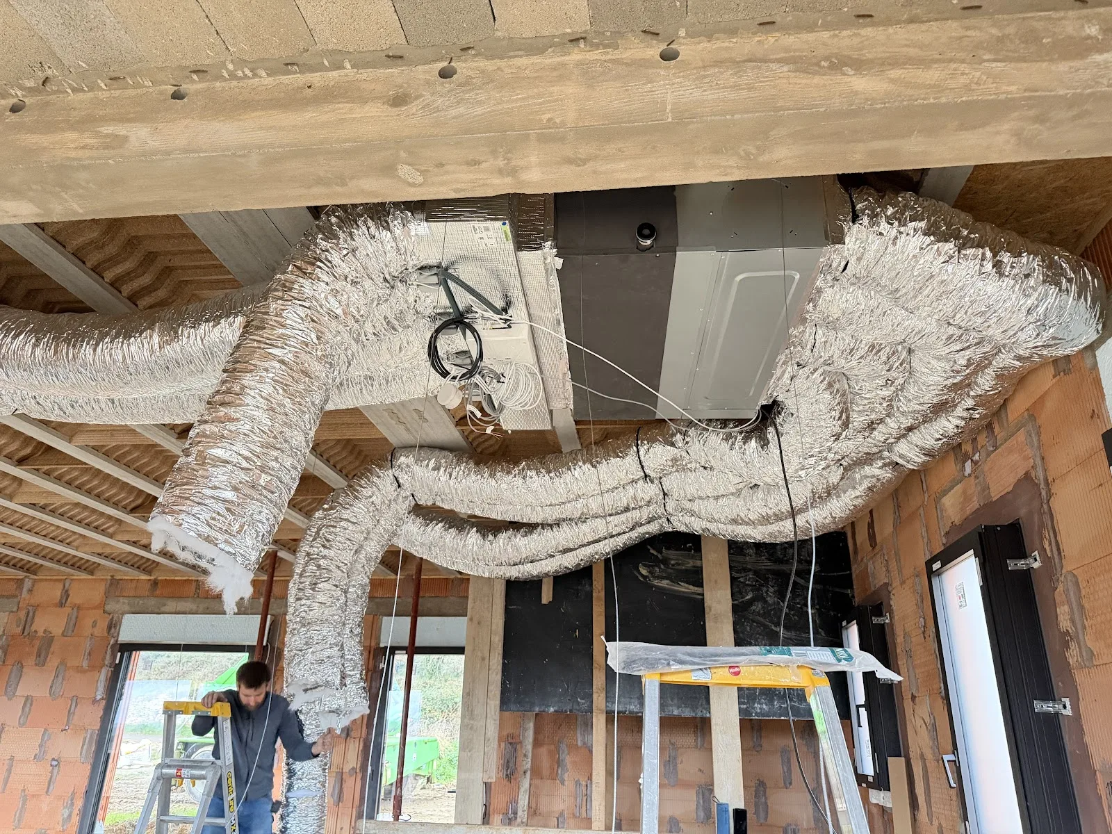Réseau de gaines de climatisation posé au plafond d'une maison en construction.
